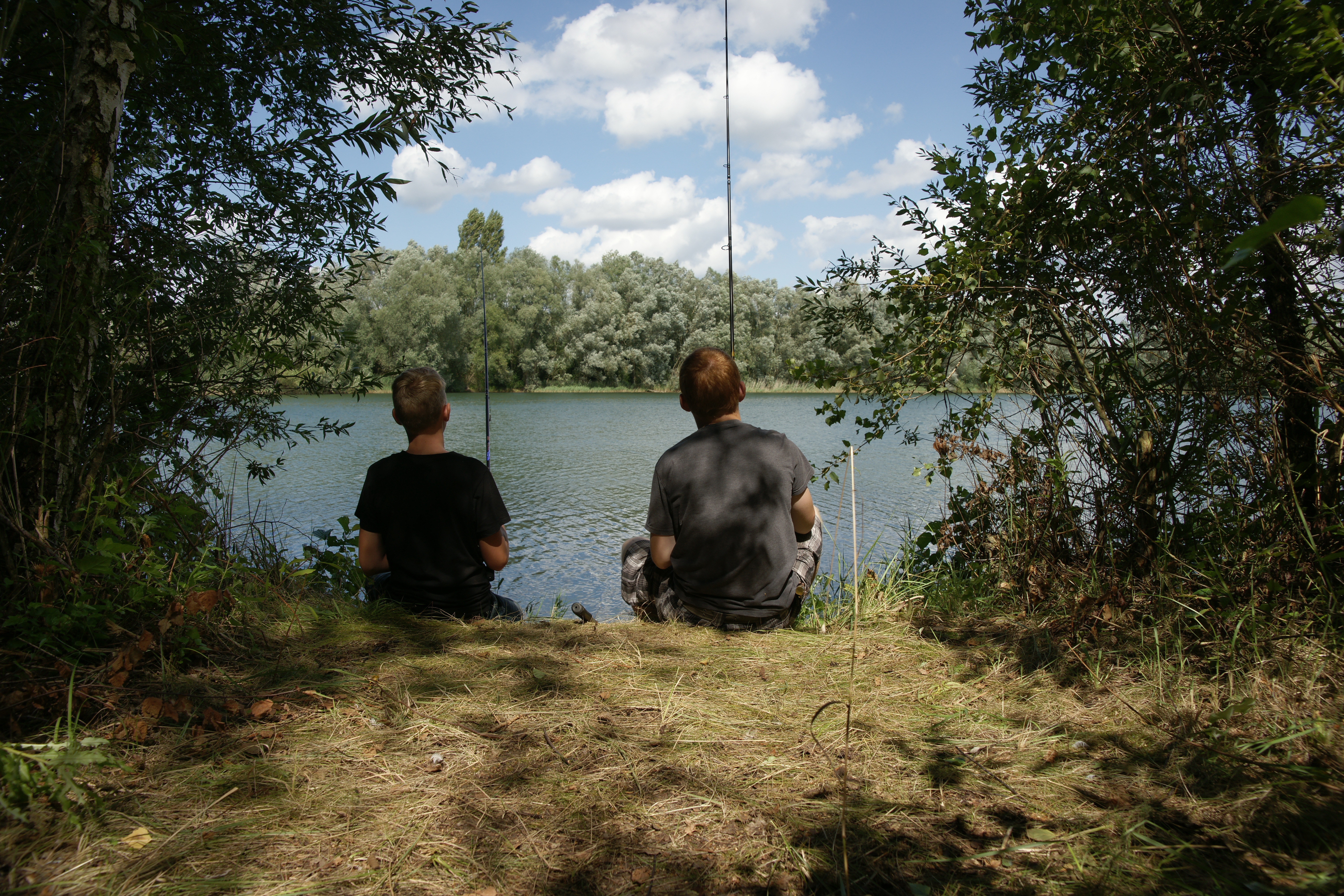 Zwei Kinder sitzen an einem See und Angeln