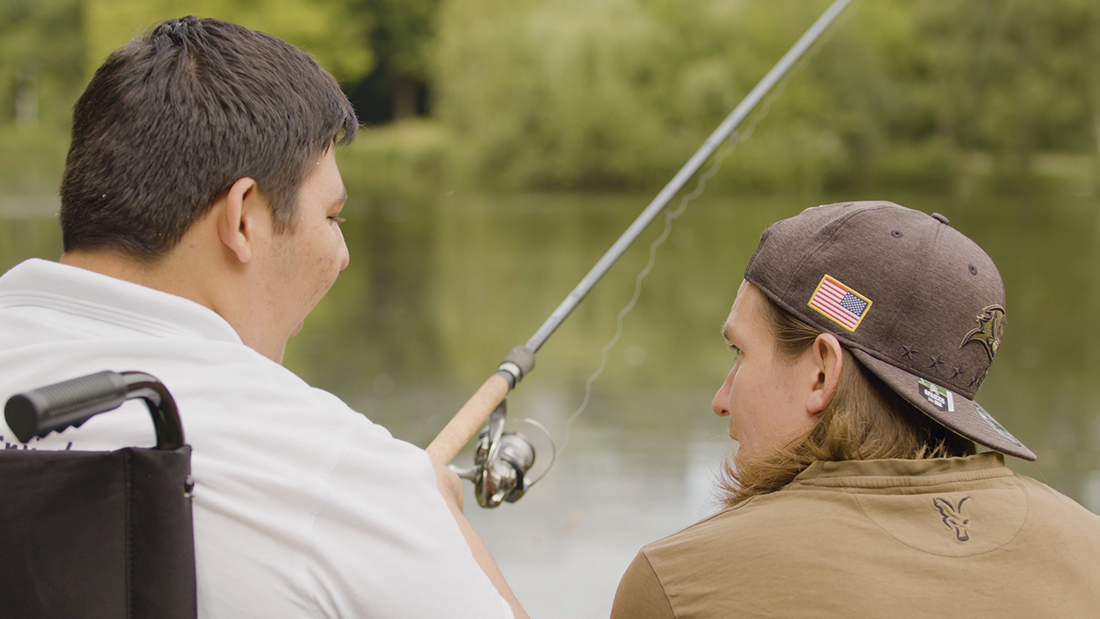 Eine Person im Rollstuhl angeln mit einer zweiten Person